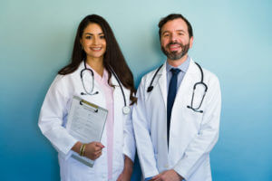Two smiling internal medicine doctors wearing white coats and stethoscopes.