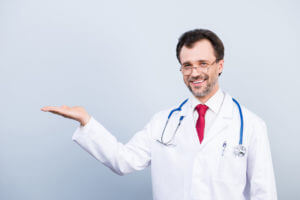 A male internal medicine doctor is wearing a medical coat and smiling.