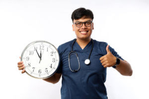 A doctor holds a clock with a thumbs-up to symbolize 24-hour, weekend, and on-call services.